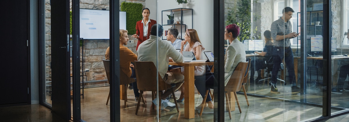 Des collaborateurs dans une salle de réunion avec un mur végétal, une femme prend la parole, souder les équipes est un passage obligé du flex office